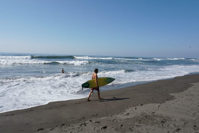person walking along beach carrying surfboard